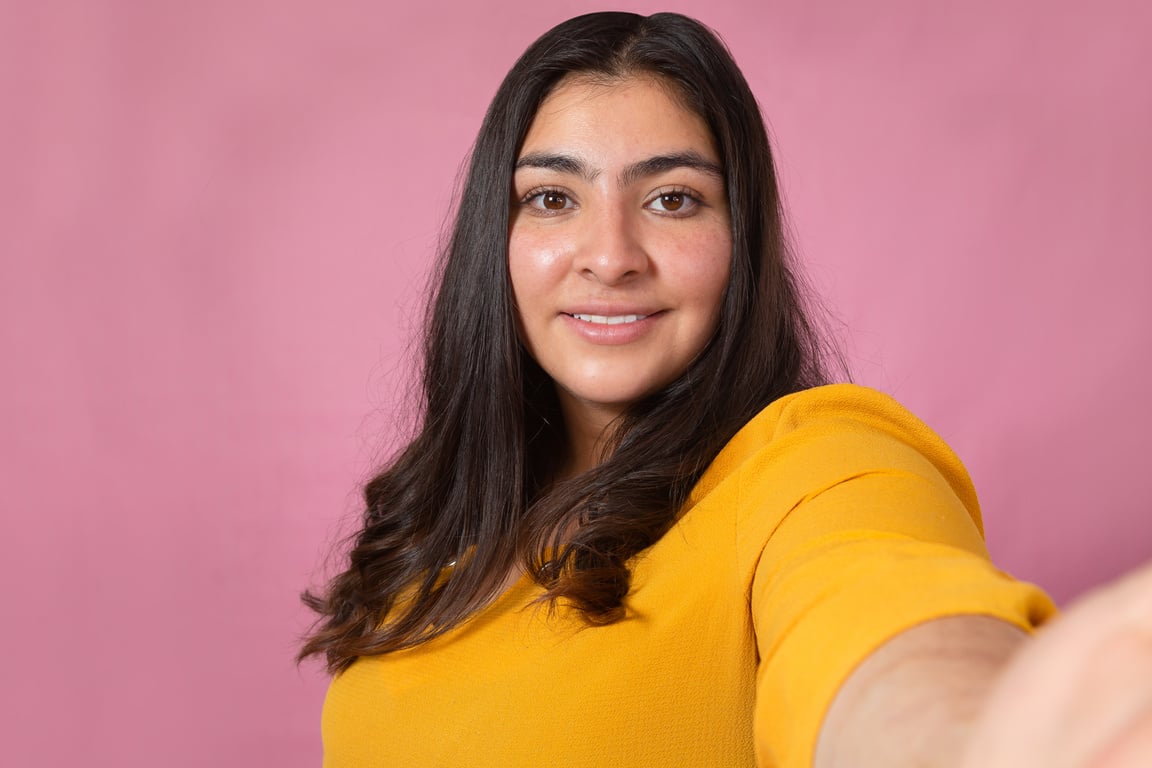 beautiful latina woman taking a selfie in studio with pink background-chubby woman